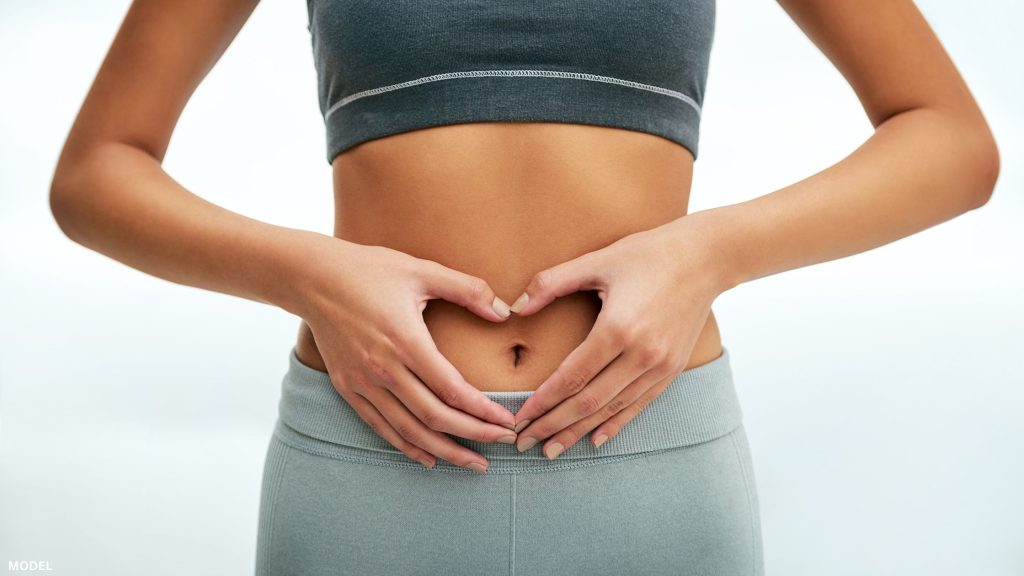 Woman holding hand heart over stomach (model)